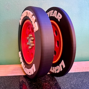 May include: Two black tires with red rims and the word "LIGHTYEAR" in white lettering. The tires are leaning against a wall. The tires have a yellow stripe around the red rim.