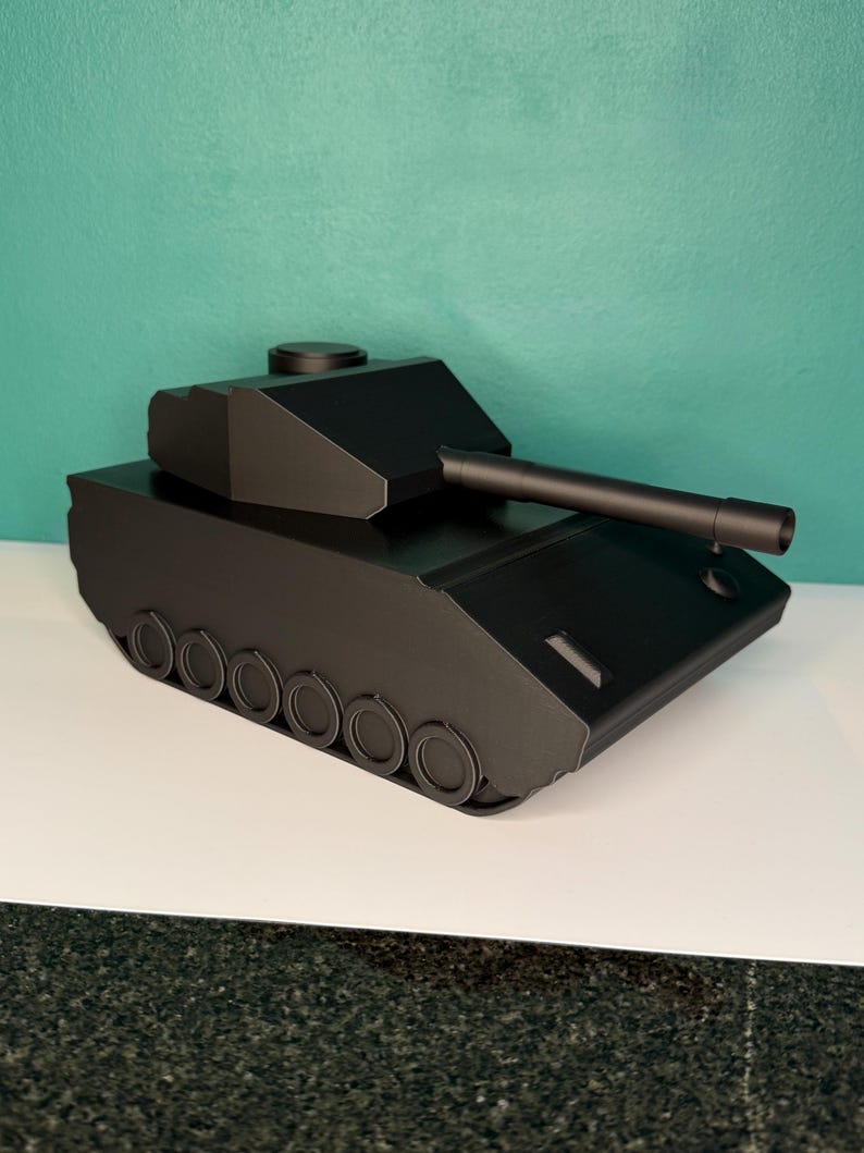 May include: A matte black toy tank featuring a rotating turret, a long barrel, and a series of circular wheels along the side. The tank has a geometric, angular design with a flat top and a smooth, solid black finish across the entire structure.