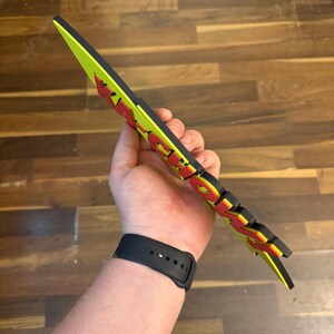 May include: A neon green and black sign with the word "KICK" in red and yellow lettering. The sign is held in a hand and appears to be made of foam or a similar material.