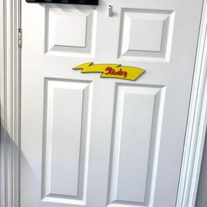 May include: A white door with a black wall-mounted rack holding four red and black decorative lights. Below, a yellow arrow-shaped sign with the name "Stanley" in red lettering.
