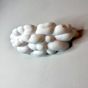 May include: A white, cloud-shaped decorative object with a textured surface. The object is made up of multiple rounded, bubble-like forms, and is mounted on a wall. The design is modern and abstract.