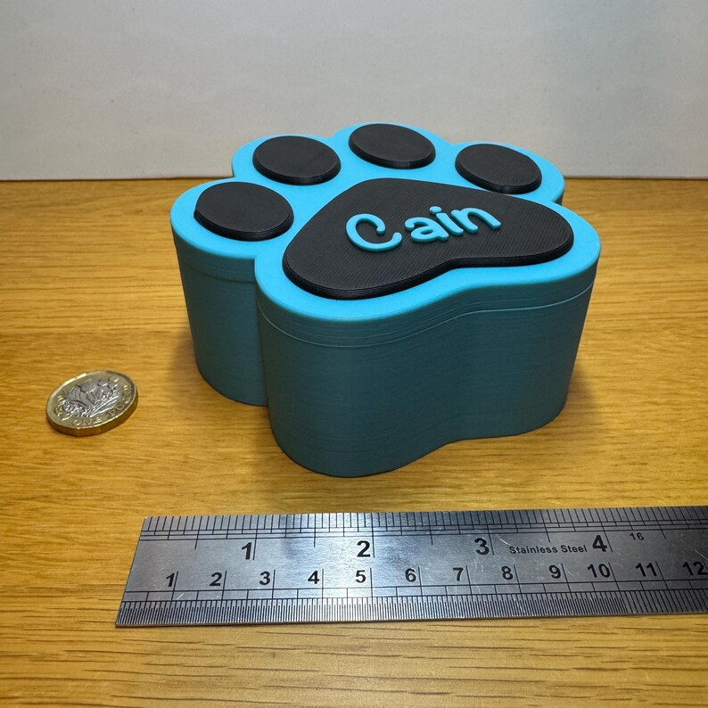 Small personalised paw print memorial box in blue and black, designed for storing pet ashes or keepsakes. Holds approx. 170ml, ideal for small pets like cats, rabbits, or toy breed dogs. Magnetic lid secures contents. Handmade Pet loss gift or urn.
