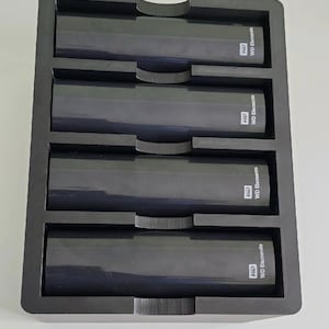 K&ouml;nnte beinhalten: Ein schwarzes, rechteckiges Aufbewahrungsfach mit vier identischen, schwarzen externen WD Elements-Festplatten, die horizontal angeordnet sind. Jedes Laufwerk tr&auml;gt das wei&szlig;e WD-Logo und den Schriftzug WD Elements auf der rechten Geh&auml;useseite.