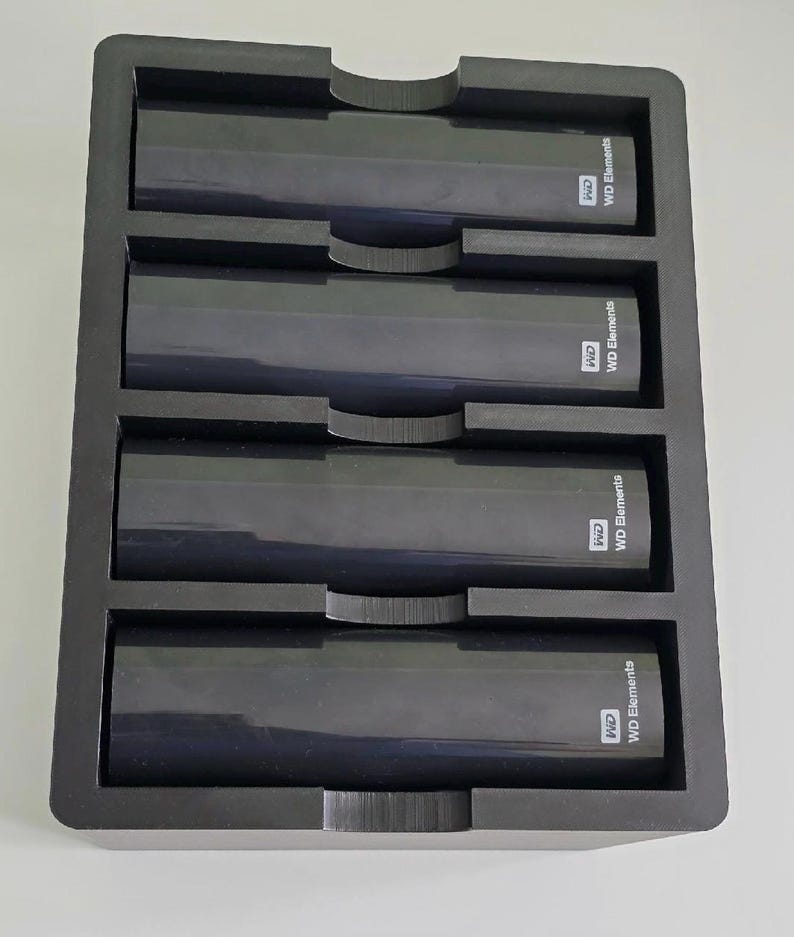 K&ouml;nnte beinhalten: Ein schwarzes, rechteckiges Aufbewahrungsfach mit vier identischen, schwarzen externen WD Elements-Festplatten, die horizontal angeordnet sind. Jedes Laufwerk tr&auml;gt das wei&szlig;e WD-Logo und den Schriftzug WD Elements auf der rechten Geh&auml;useseite.
