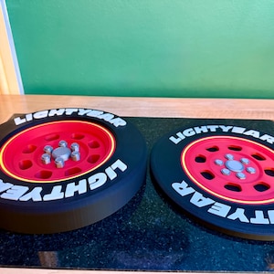 May include: Two black and red decorative wheels with the word "LIGHTYEAR" in white lettering. The wheels have a red center with silver bolts and a yellow rim. The wheels are on a black surface.