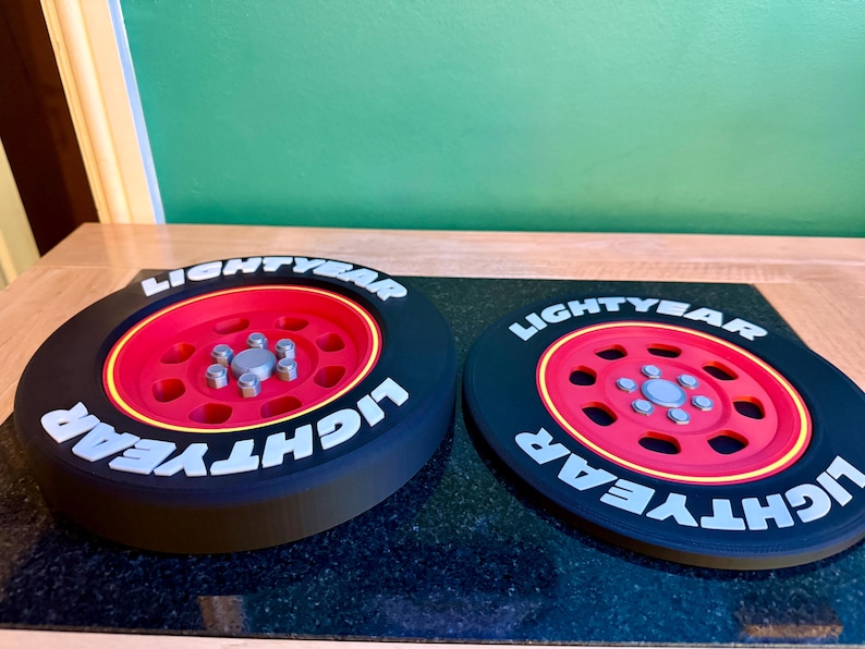 May include: Two black and red decorative wheels with the word "LIGHTYEAR" in white lettering. The wheels have a red center with silver bolts and a yellow rim. The wheels are on a black surface.