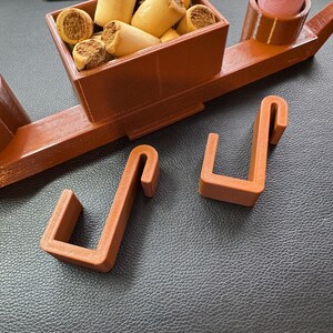 Adjustable hooks for dog crate organiser in oak wood effect. Designed to securely attach the organiser to crate gaps without tools. Ideal for holding leads, poo bags, treats, and tennis balls. Perfect for dog walkers and pet owners on the go.