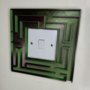 A 3D-printed, decorative light switch cover with a maze-like design. The intricate pattern adds a unique and playful touch to any room, making it both functional and visually appealing for various settings.