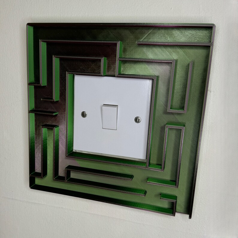A 3D-printed, decorative light switch cover with a maze-like design. The intricate pattern adds a unique and playful touch to any room, making it both functional and visually appealing for various settings.