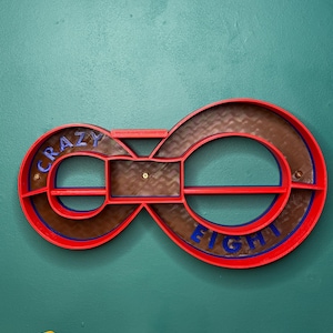 May include: A red and brown infinity-shaped shelf with the words "CRAZY EIGHT" in blue. The shelf is mounted on a teal wall. Several toy cars are lined up below the shelf.