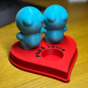 Personalised 3D printed tealight holder featuring cute bubble people figurines on a heart-shaped base. Customisable with names, perfect as a romantic Valentine’s gift, anniversary present, or home decor. Designed for use with LED tealights.