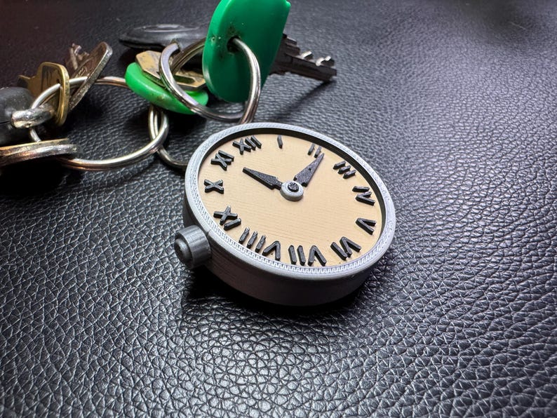 May include: A silver-coloured pocket watch with Roman numeral markings on a beige face. The watch is attached to a set of keys with green and silver keychains.