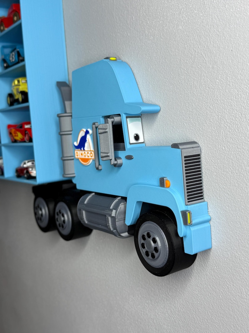 May include: A light blue toy truck with a trailer, mounted on a wall. The truck features black tires, a gray grill, and the "Dinoco" logo. The trailer has shelves holding miniature toy cars.