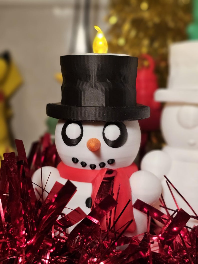 Adorable 3D-printed snowman tealight holders in white and multicolour, featuring festive designs with hats, scarves, and LED tealights. Perfect as Christmas decorations or gifts, displayed on a table with holiday-themed backdrops.
