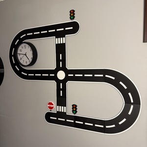 May include: A black and white road-themed wall decoration with a clock, stop signs, and traffic lights. The road design includes curves, intersections, and white dashed lines. The clock has black hands and a white face.