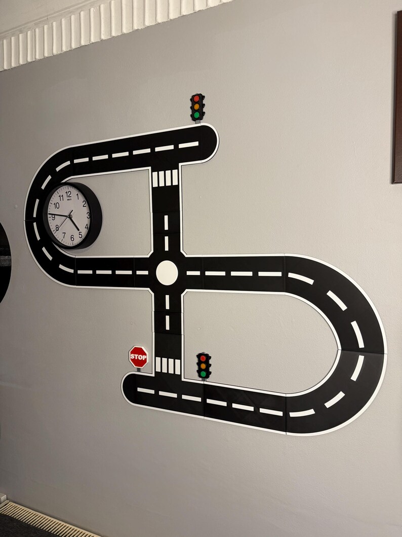 May include: A black and white road-themed wall decoration with a clock, stop signs, and traffic lights. The road design includes curves, intersections, and white dashed lines. The clock has black hands and a white face.