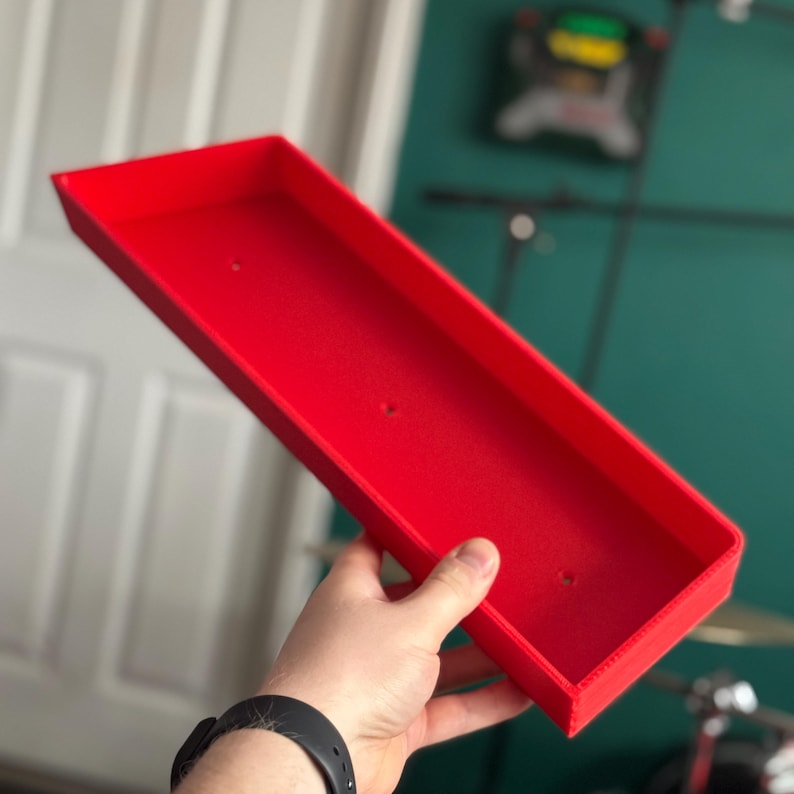 May include: A bright red plastic tray with rounded edges and three small holes. The tray is held in a person's hand.