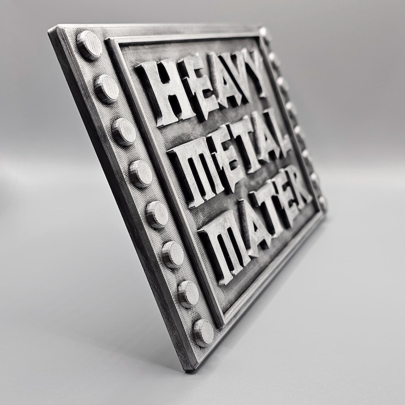 Peut inclure: Panneau rectangulaire argent&eacute; avec les mots "HEAVY METAL MATER" en lettres en relief. Le panneau a une bordure rivet&eacute;e avec des accents circulaires. Le panneau est inclin&eacute;, mettant en valeur son design en trois dimensions.