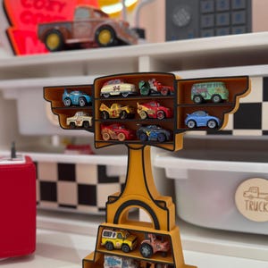 Puede incluir: Una estanter&iacute;a amarilla con forma de trofeo, llena de coches de juguete en miniatura de varios colores. La estanter&iacute;a tiene varios niveles para guardar los coches, y el dise&ntilde;o general recuerda el tema de las carreras.