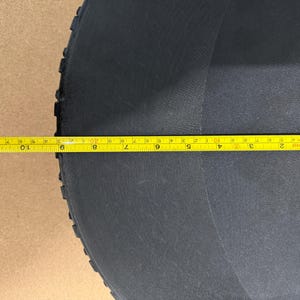 Może przedstawiać: Czarny, p&oacute;łkolisty przedmiot o teksturowanej powierzchni. Ż&oacute;łta miarka leży na przedmiocie, wskazując pomiar około 28 cm. Przedmiot wydaje się być wykonany z trwałego materiału.