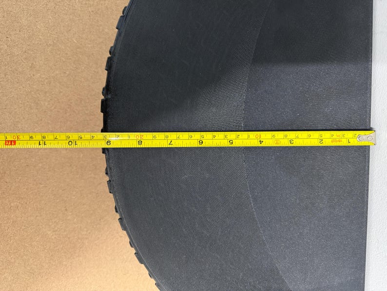 Może przedstawiać: Czarny, p&oacute;łkolisty przedmiot o teksturowanej powierzchni. Ż&oacute;łta miarka leży na przedmiocie, wskazując pomiar około 28 cm. Przedmiot wydaje się być wykonany z trwałego materiału.