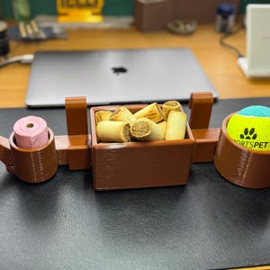 Full view of brown PETG 3D-printed dog crate organiser. Holds treats, a tennis ball, and poo bags with slots for two leads. Heat-resistant and durable, it hooks onto crates without tools. Customisable and perfect for dog walkers and pet owners.