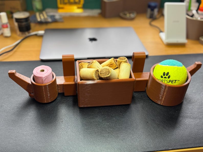 Full view of brown PETG 3D-printed dog crate organiser. Holds treats, a tennis ball, and poo bags with slots for two leads. Heat-resistant and durable, it hooks onto crates without tools. Customisable and perfect for dog walkers and pet owners.