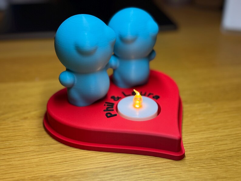 Personalised 3D printed tealight holder featuring cute bubble people figurines on a heart-shaped base. Customisable with names, perfect as a romantic Valentine’s gift, anniversary present, or home decor. Designed for use with LED tealights.
