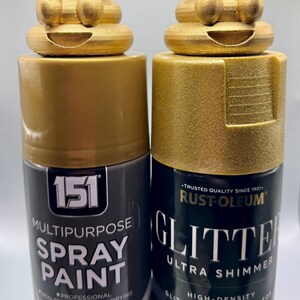 Two gold glittery 3D-printed poop emoji figurines sitting on top of gold spray paint and spray glitter cans. The cans show the paints used to achieve the metallic finish. Fun and eco-friendly decor made from recycled plastic.