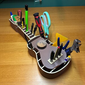 Guitar desk caddy filled with tools and stationery, showcasing its multiple storage sections. Printed in wood-tone PLA, blending style with function.