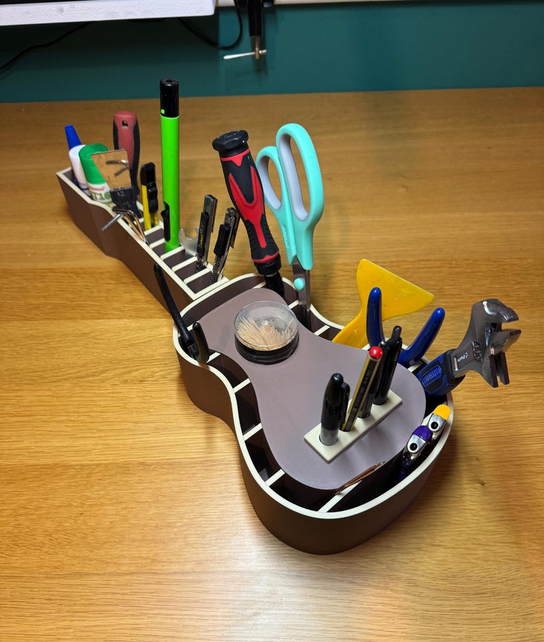 Guitar desk caddy filled with tools and stationery, showcasing its multiple storage sections. Printed in wood-tone PLA, blending style with function.