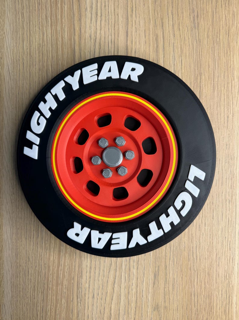 May include: A black and red decorative wheel with the text "LIGHTYEAR" in white. The wheel has a red center with silver bolts and a yellow stripe around the rim. The design is reminiscent of a race car wheel.