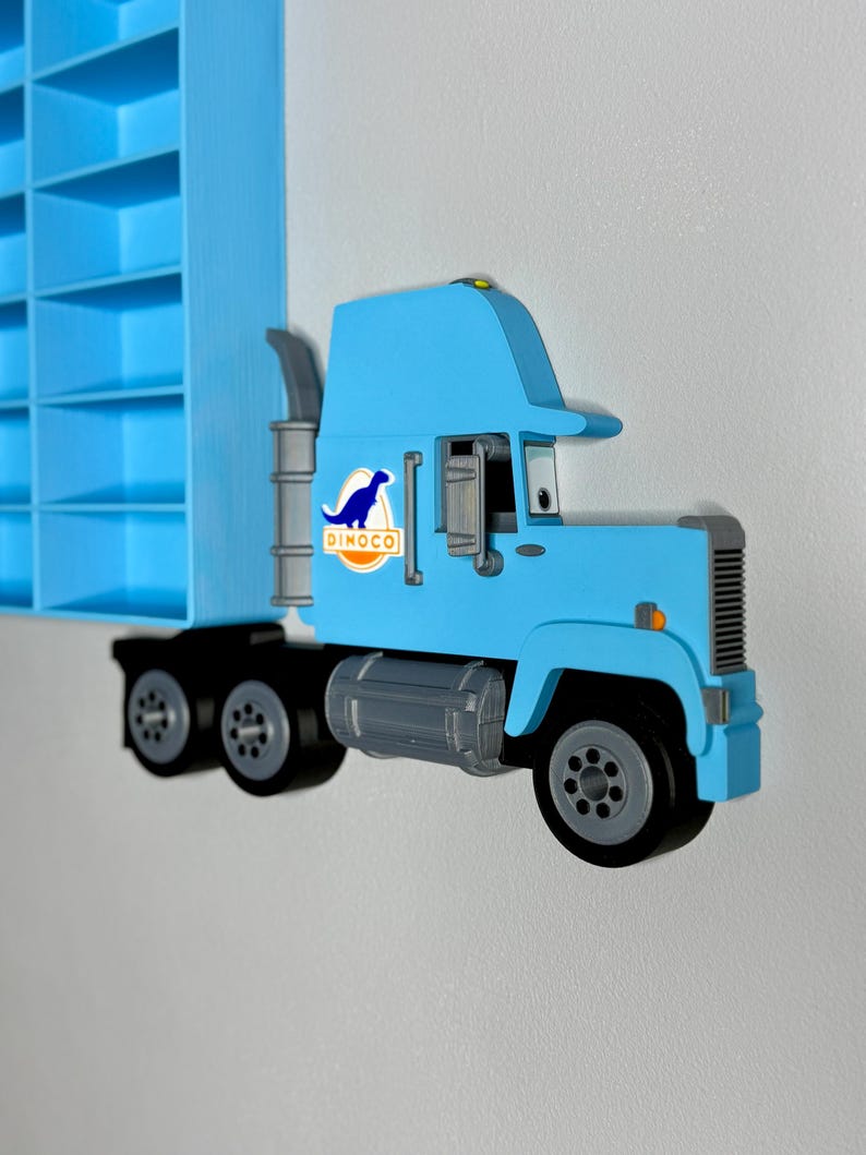 May include: A light blue toy truck with black wheels and a gray exhaust pipe. The truck features the Dinoco logo on the side. A blue shelf is visible in the background.