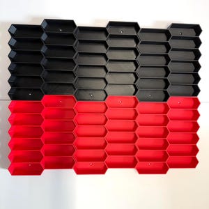 May include: A modular storage organizer featuring a grid of interconnected hexagonal compartments. The top half consists of black hexagonal bins, while the bottom half features red hexagonal bins. Each individual compartment has a small circular hole.