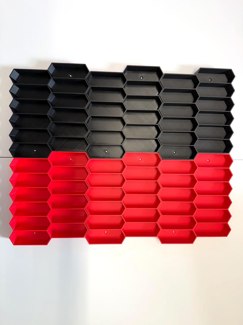 May include: A modular storage organizer featuring a grid of interconnected hexagonal compartments. The top half consists of black hexagonal bins, while the bottom half features red hexagonal bins. Each individual compartment has a small circular hole.