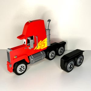 May include: A red toy truck with the number "95" in yellow lightning bolts on the side. The truck has a silver grill, exhaust pipe, and fuel tanks. The black trailer is detached.