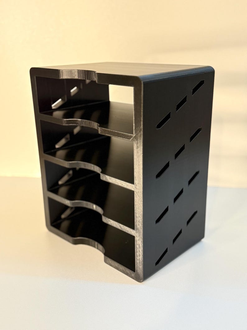 May include: A black wooden wine rack with a rectangular shape. The rack has multiple shelves with curved edges to hold wine bottles. The sides of the rack have a series of angled cutouts. The edges of the rack have a silver finish.
