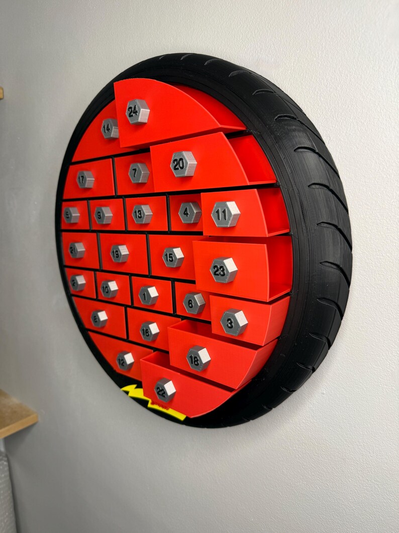 May include: A red and black advent calendar shaped like a tire. The calendar has 24 numbered compartments with silver-colored bolt-shaped knobs. The tire has a black rubber tread.