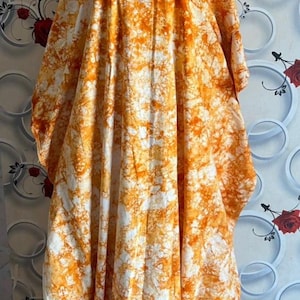 May include: A long, flowing orange and white tie-dye dress with a white collar and a white head covering.
