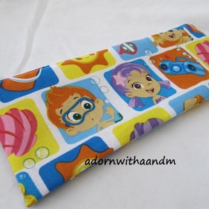 Puede incluir: Un estuche rectangular con cierre de cremallera. El diseño colorido presenta personajes de dibujos animados, soles y otras imágenes de temática acuática sobre un fondo blanco. El estuche mide unos 20 cm de largo.