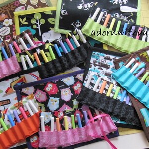 May include: A collection of colorful chalk holders made from patterned fabric. Each holder is filled with chalk sticks in various colors. The fabric designs include owls, trees, and construction vehicles. Some holders have ribbon closures.