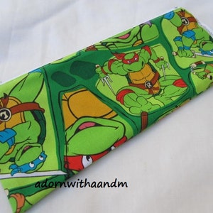 May include: Green rectangular pencil case featuring a repeating pattern of Teenage Mutant Ninja Turtles in various action poses. The case has a white zipper and is made of fabric. The background is white.