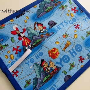 Può includere: Un oggetto di tessuto blu con un motivo a tema pirata con Capitan Uncino, Jake e altri personaggi. Il design include forzieri, mappe e le parole "Yo Ho" e "Let's Go!" Un bordo blu incornicia il tessuto.