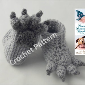May include: A pair of grey crocheted baby booties shaped like a paw print. The booties have a textured surface and are made with a soft yarn.