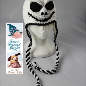 May include: White crocheted hat with a black and white face resembling Jack Skellington from the Nightmare Before Christmas. The hat has long black and white striped ties.