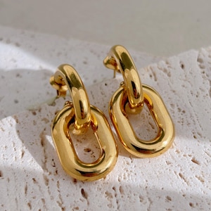 Peut inclure: Une paire de boucles d'oreilles dorées à maillons de chaîne épais. Chaque boucle d'oreille présente un grand maillon de forme ovale relié à un maillon plus petit et incurvé qui se fixe à la tige d'oreille. Les boucles d'oreilles ont une surface polie et réfléchissante.