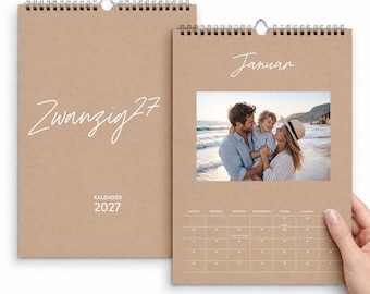 Op de afbeelding: Twee wandkalenders van bruin kraftpapier met spiraalbinding. De linker omslag toont de tekst Zwanzig27 en Kalender 2027. De rechter kalender toont de maand Januar met een foto van drie personen op een strand en een rasterindeling.