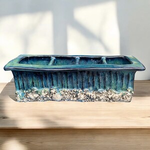 Puede incluir: Un macetero de cerámica azul con tres compartimentos, que presenta un diseño texturizado con forma de concha alrededor del borde inferior.