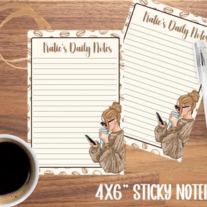May include: Two 4x6 inch sticky notepads with the text "Katie's Daily Notes" and a coffee bean border. Each notepad features an illustration of a woman with sunglasses holding a phone and a coffee cup. A pen rests on the right notepad. A cup of coffee is in the lower left.