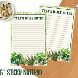 May include: Two 4x6 inch sticky notepads with the text "Tyla's Daily Notes" in green. The notepads have a lined interior and a botanical design at the bottom. A small bowl of gold binder clips is in the upper left corner.